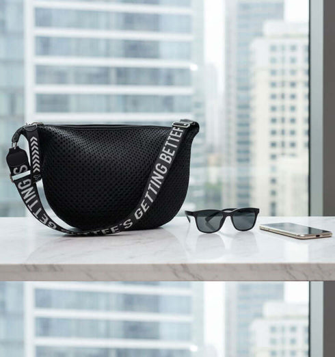 פאוץ' טרנדי בגוון שחור עם רצועות מתכווננות, משולב עם משקפי שמש וטלפון על שולחן בעיצוב מודרני.