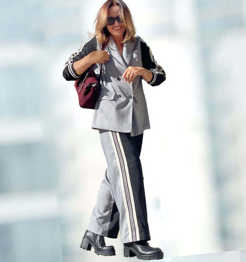 אישה לובשת חליפת כותנה מכופתרת בסגנון ספורט אלגנט בגווני אפור ושחור עם תיק וכובע.