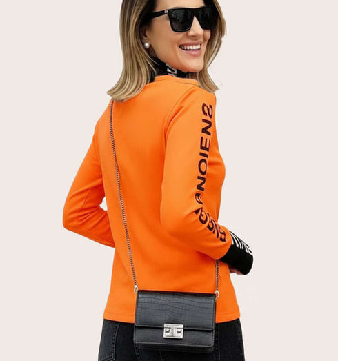 טישרט ארוכת שרוולים בגוון כתום, עם שרוולים וצווארון שחורים מודפסים, בשילוב עם תיק קטן.