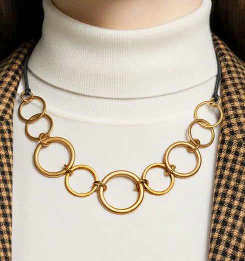 שרשרת טבעות זהב מקושרות בגדלים שונים מעוצבת עם טבעות זהב קלילות על רקע בגדים מודרניים.
