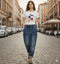 אישה בג'ינס ווינטג' מובחר בגזרה גבוהה עם כיסים צדדיים, צועדת ברחוב בעיר אירופאית.