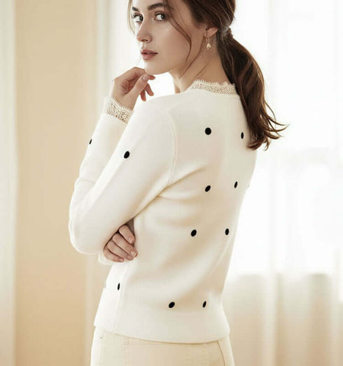 סריג קרדיגן לבן מנוקד בשחור, כפתורים לבנים ותחרה לבנה בחזה ובשוליים, מראה אלגנטי ונעים.
