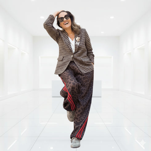 אישה smiling בלבוש אופנתי, ג'אקט כותנת צמר בצבעים חומים משובצים עם מכנסיים באפרסק עם פסים אדומים.