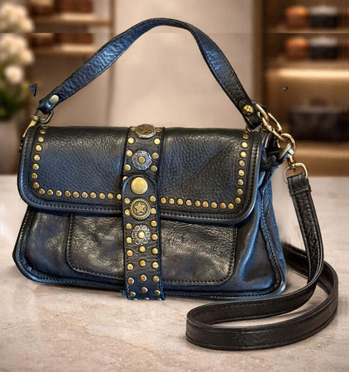 תיק עור שחור מובחר עם ניטים נחושתיים ורצועה תואמת לכתף על שולחן, בעיצוב ייחודי ואלגנטי.