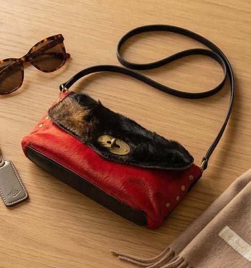 תיק צד מעורות פרווה צבעוני עם רצועת עור שחורה, בשילוב אדום ושחור, מראה יוקרתי.