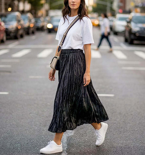 חצאית סאטן משי שחורה עם קימוטים, נראית באופנת רחוב עם חולצה לבנה ונעלי ספורט.