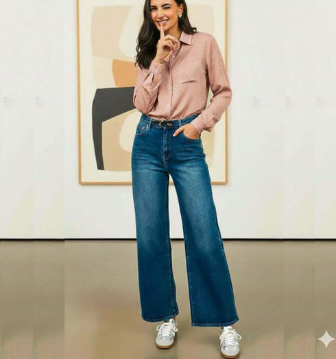 אישה לבושה בג'ינס משופשף עם מותן גבוה וסגנון פדלפון, עומדת בסלון מודרני.